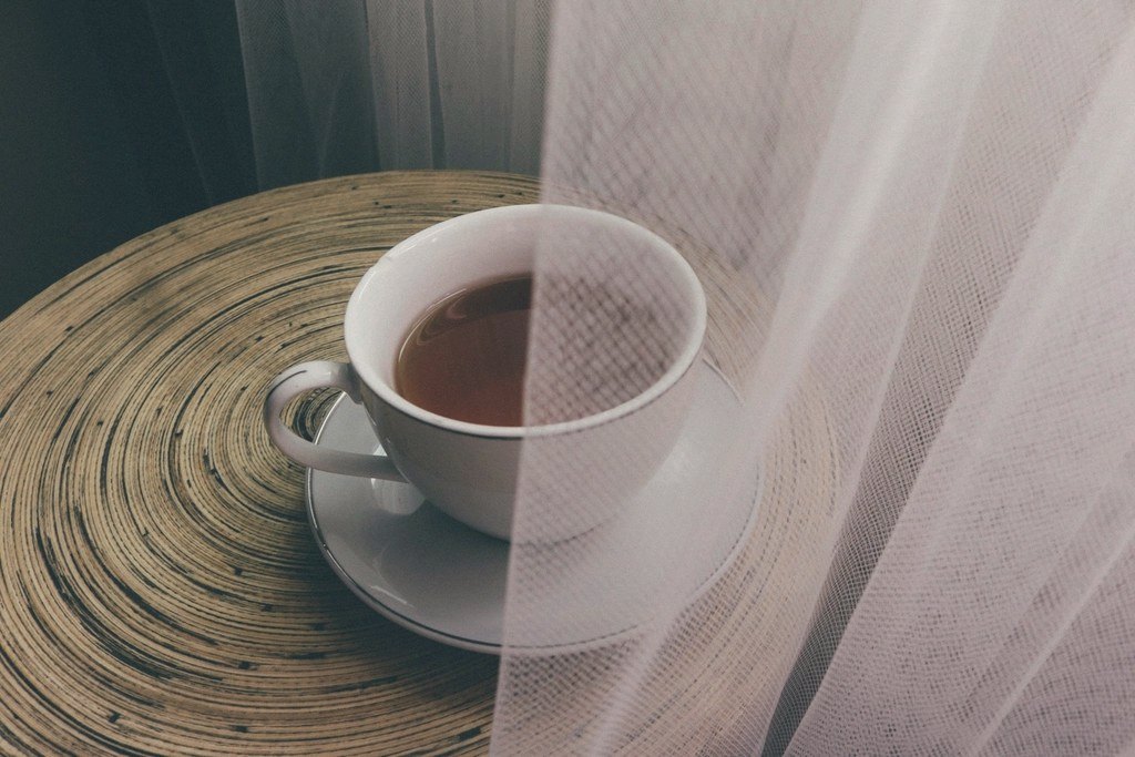 Une tasse de thé sur une table ronde, à demi voilée par un rideau léger.